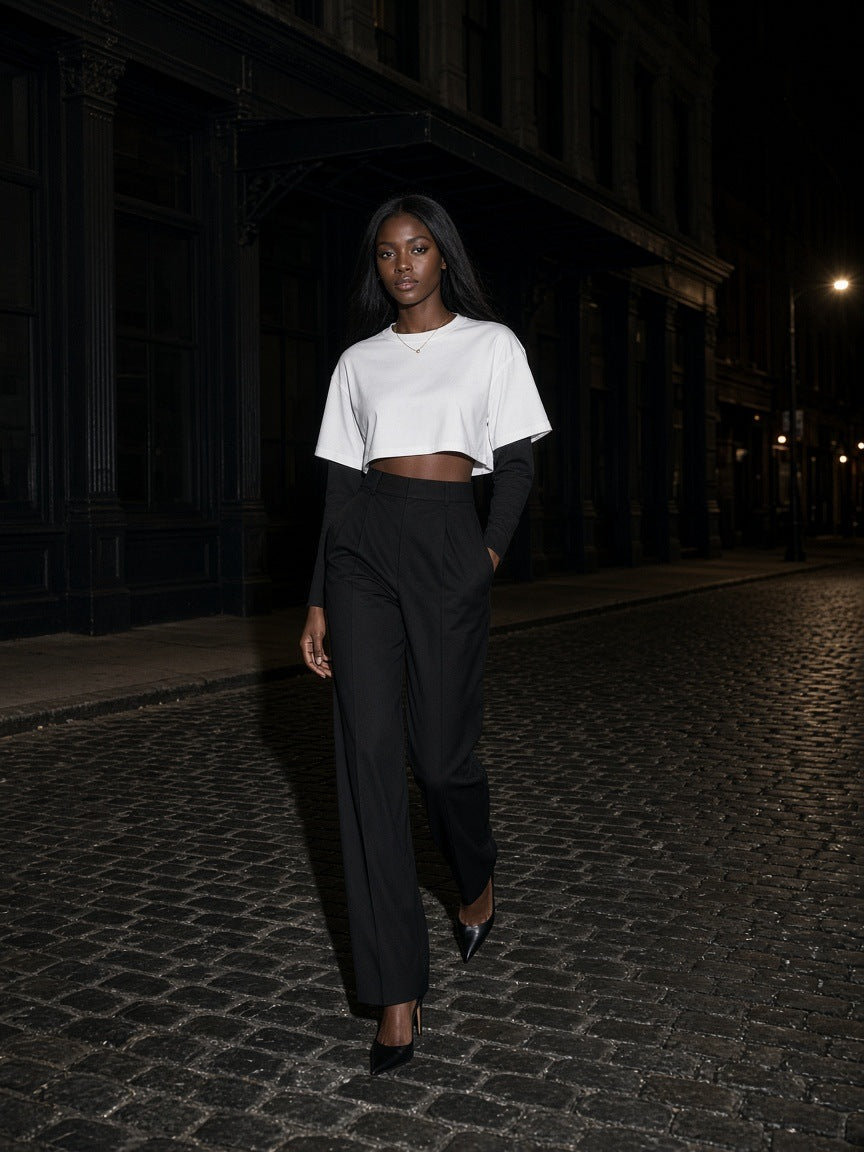Woman in the Marcel Afters Layered Contrast Sleeve Cotton T-Shirt in White with Black walking a cobblestone street in Tribeca, New York at night