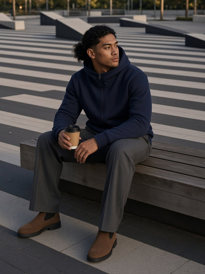 Man in the Men's Essential Heavyweight High Neck Zip-Up Hoodie in Navy Blue with a coffee on a bench in Superkilen park, Copenhagen, in the morning