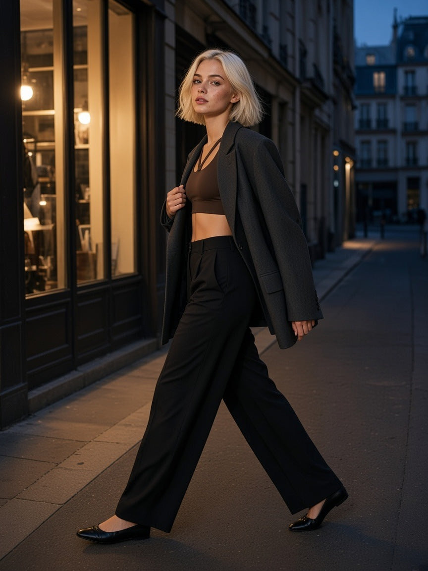 Woman in the Strappy Criss-Cross Sports Bra in Brown with an open charcoal blazer and black wide trousers, crossing the Passage des Panoramas in Paris at night