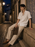 Man in a white lightweight cotton short sleeve shirt and ecru trousers on a tiled Lisbon street at night