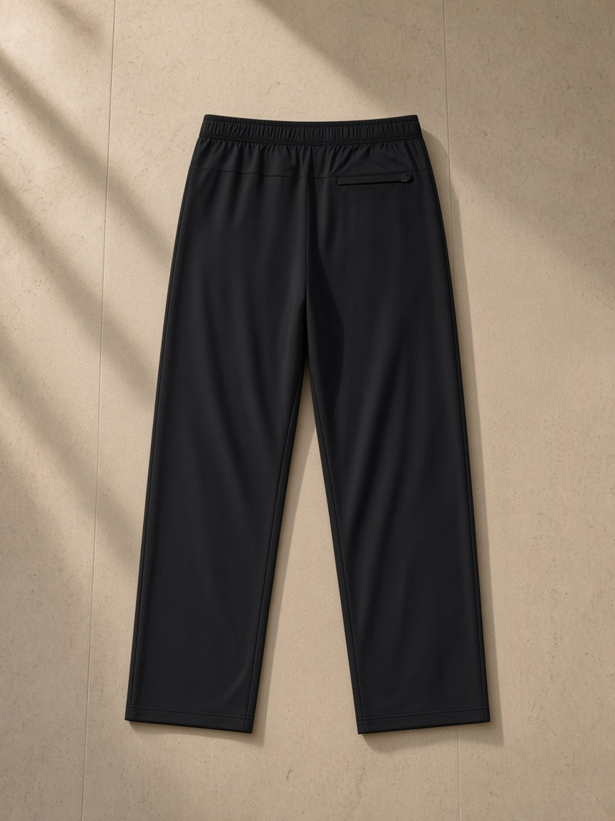 Lightweight Tapered Track Pants in Black, laid flat on pale limestone, back view