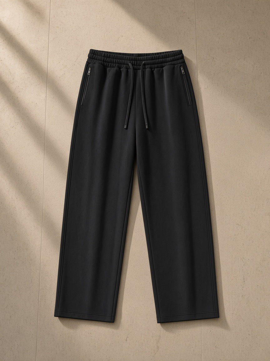 Lightweight Tapered Track Pants in Black, laid flat on pale limestone