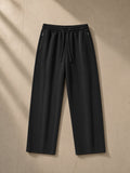 Lightweight Tapered Track Pants in Black, laid flat on pale limestone