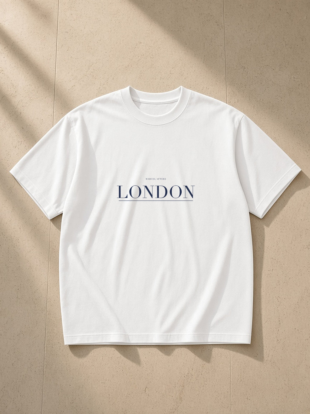London heavyweight drop-shoulder tee in White laid flat on pale limestone, the London plate across the chest
