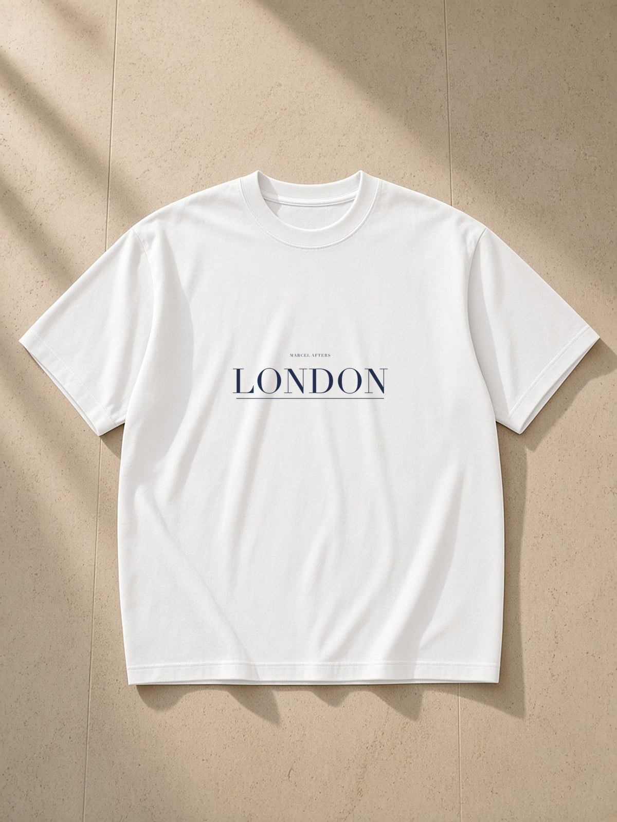 London heavyweight drop-shoulder tee in White laid flat on pale limestone, the London plate across the chest