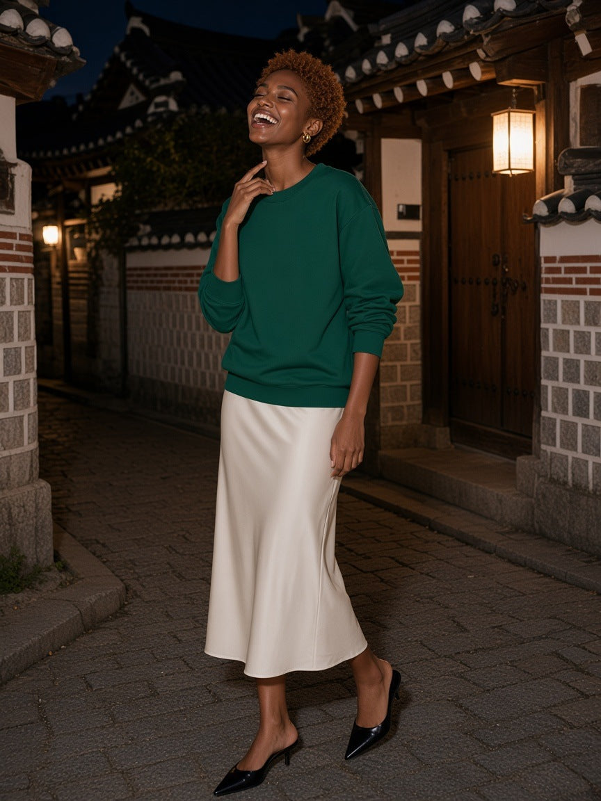 Woman in the Marcel Afters loose crewneck sweatshirt in Dark Green standing on a whitewashed stair on Mykonos at dusk