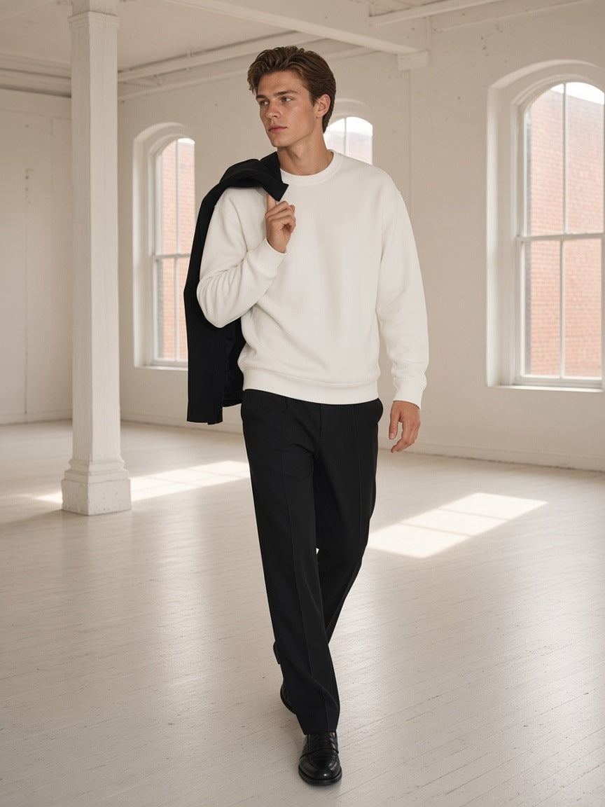 Man in the Loose Crewneck Sweatshirt in White with black trousers and loafers, standing in a Tribeca loft in New York in the morning