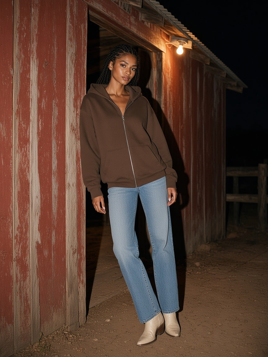 Woman in the Marcel Afters loose solid full zip hoodie in Coffee leaning in a barn doorway on a Wyoming ranch at night
