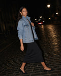 Woman crossing a wet cobbled street at night in the Women's Slim Sleeveless Dress in Black with a blue vintage wash denim jacket and black flats, looking back