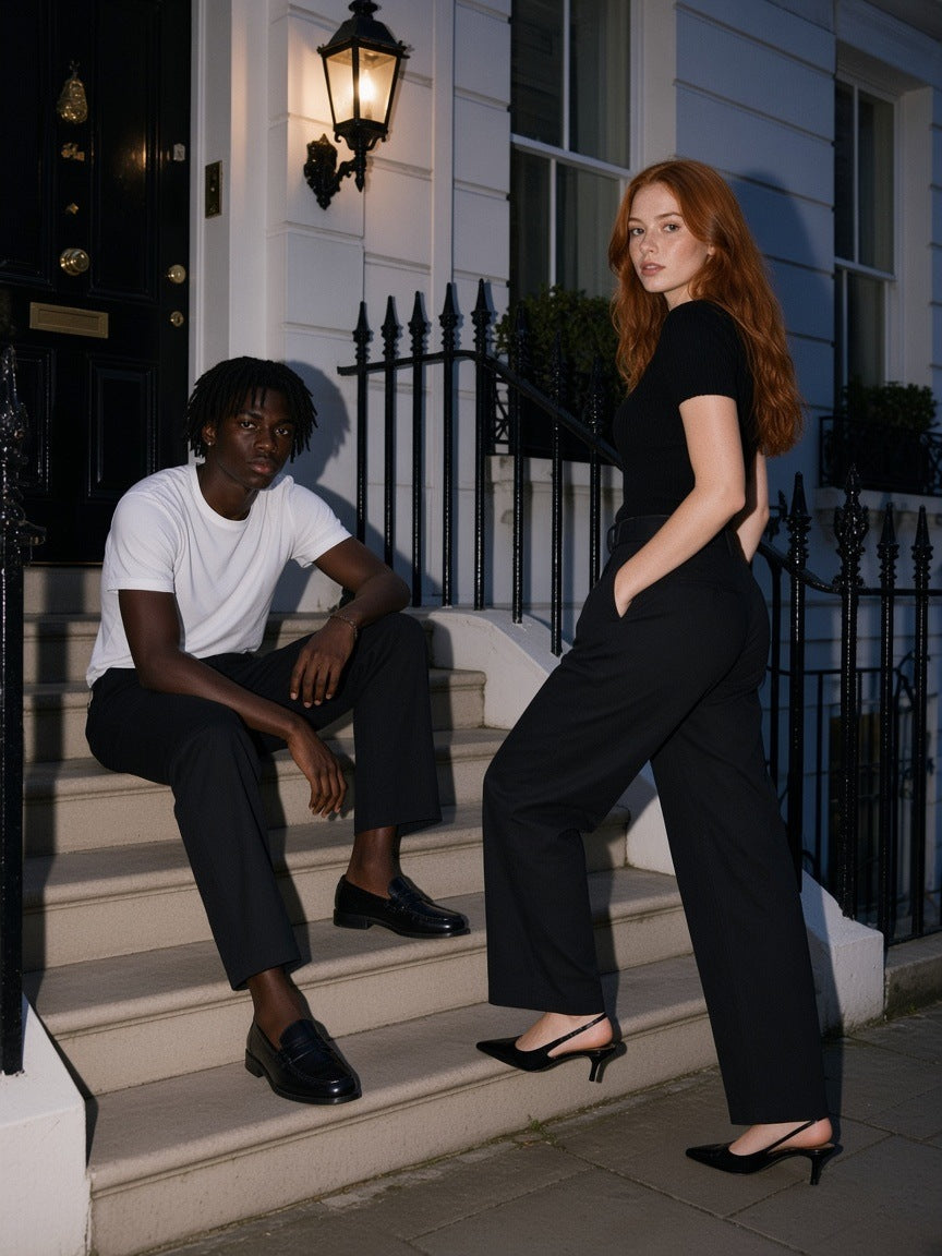 Marcel Afters Belted Barrel-leg Chino Pants in Black, worn by a man and a woman, seated and standing on white townhouse steps at dusk