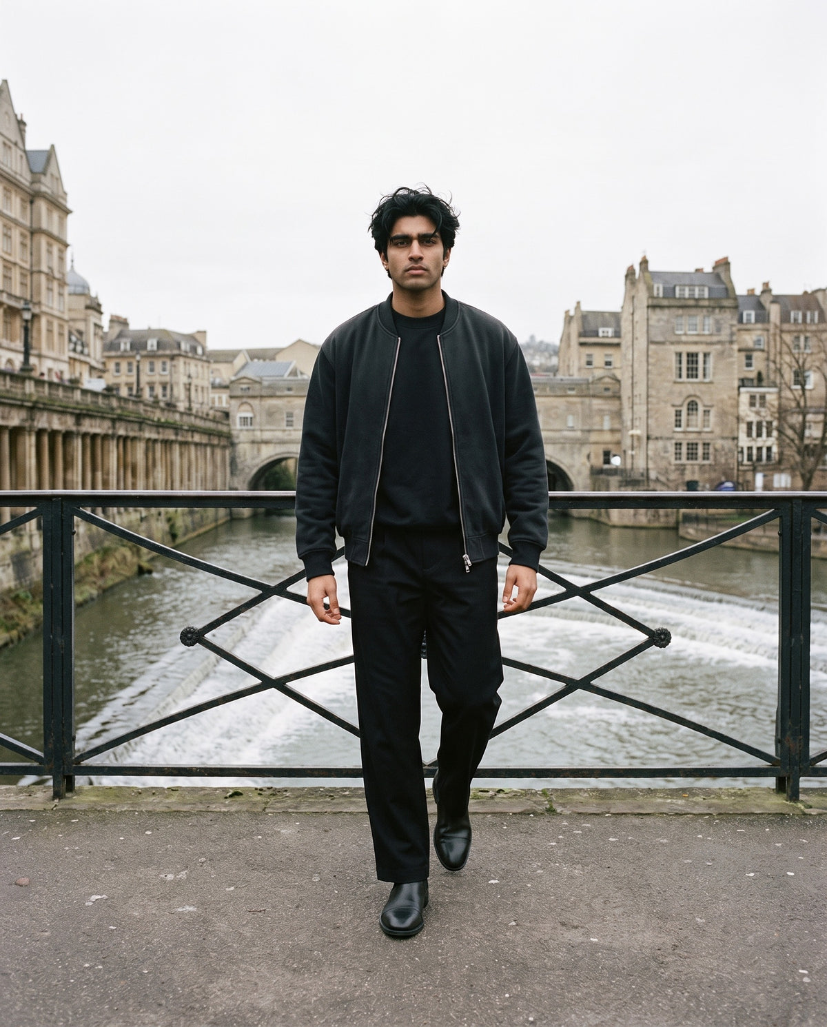 Man wearing The Smoking Room Chelsea Boot with the Essential Heavyweight Dolman Sleeve Boxy Sweatshirt in Black, Adjustable Waist Straight-Leg Pants in Black, Sun Fade Heavyweight Baseball Jacket in Black. Cold City, Autumn–Winter 2026 campaign