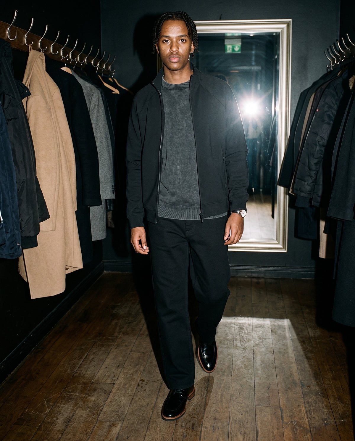 Man wearing The Concierge Derby with the Mineral Wash Oversized Sweater in Black, Heavyweight Straight-Leg Trousers in Black, Zip-Pocket Stand Collar Jacket in Black. Dinner at Nine, Autumn–Winter 2026 campaign