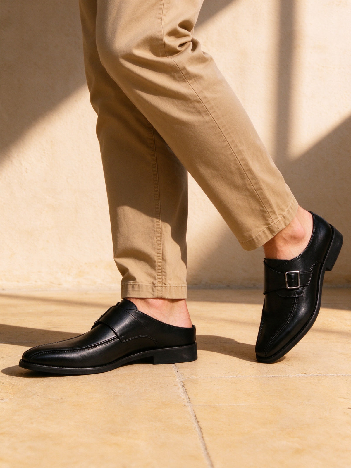 The Cloakroom Monk in black on foot, pale stucco wall and sun-warmed stone pavement