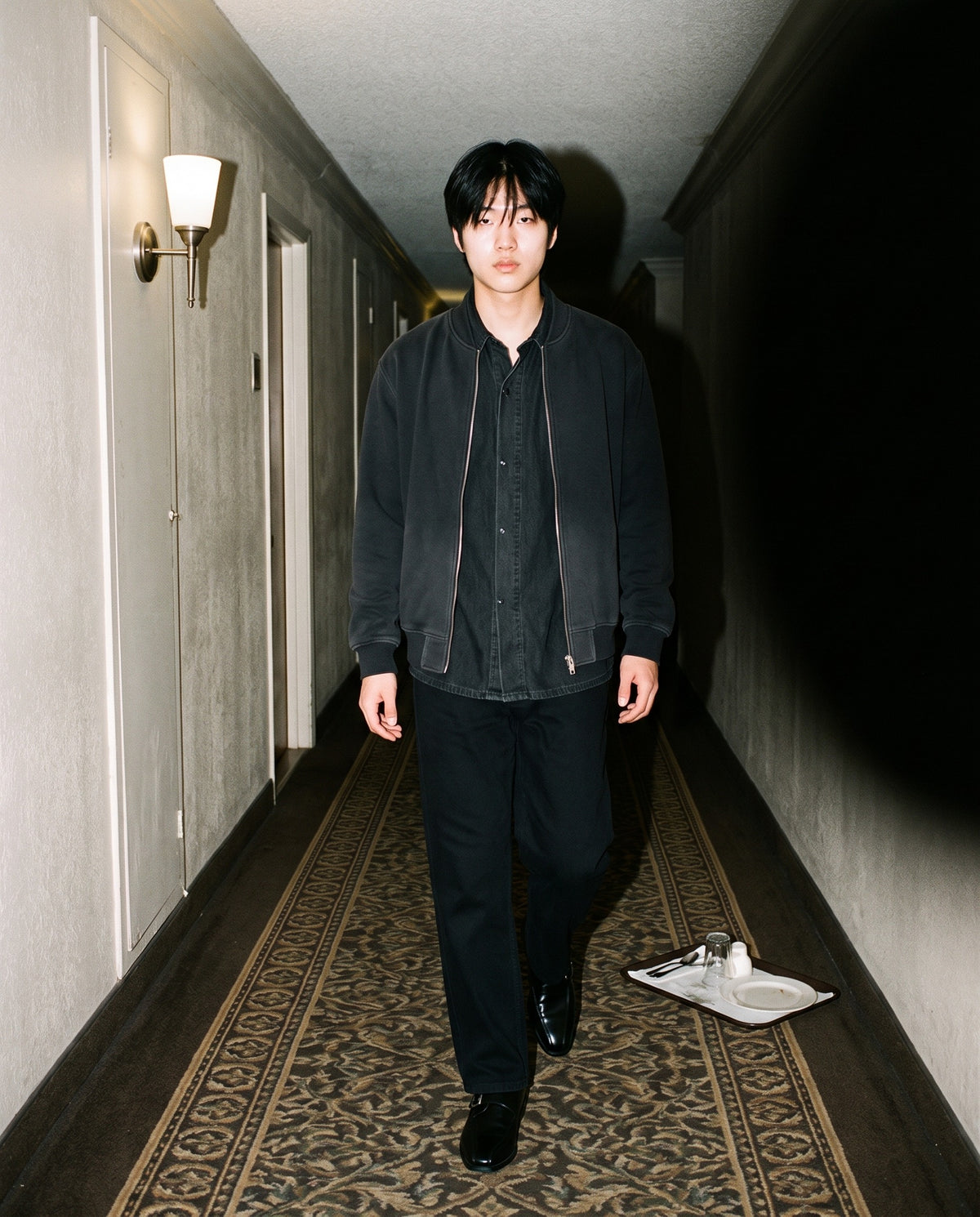 Man wearing The Cloakroom Monk with the Vintage Wash Lyocell Shirt in Black, Heavyweight Cotton Straight-Leg Pants in Black, Sun Fade Heavyweight Baseball Jacket in Black. After Dark, Autumn–Winter 2026 campaign