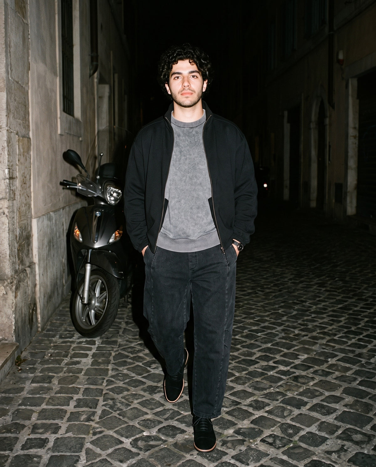 Man wearing The Velvet Rope Oxford with the Mineral Wash Oversized Sweater in Gray, Mineral Wash Barrel Leg Pants in Black, Essential Heavyweight Stand Collar Jacket in Black. Dinner at Nine, Autumn–Winter 2026 campaign