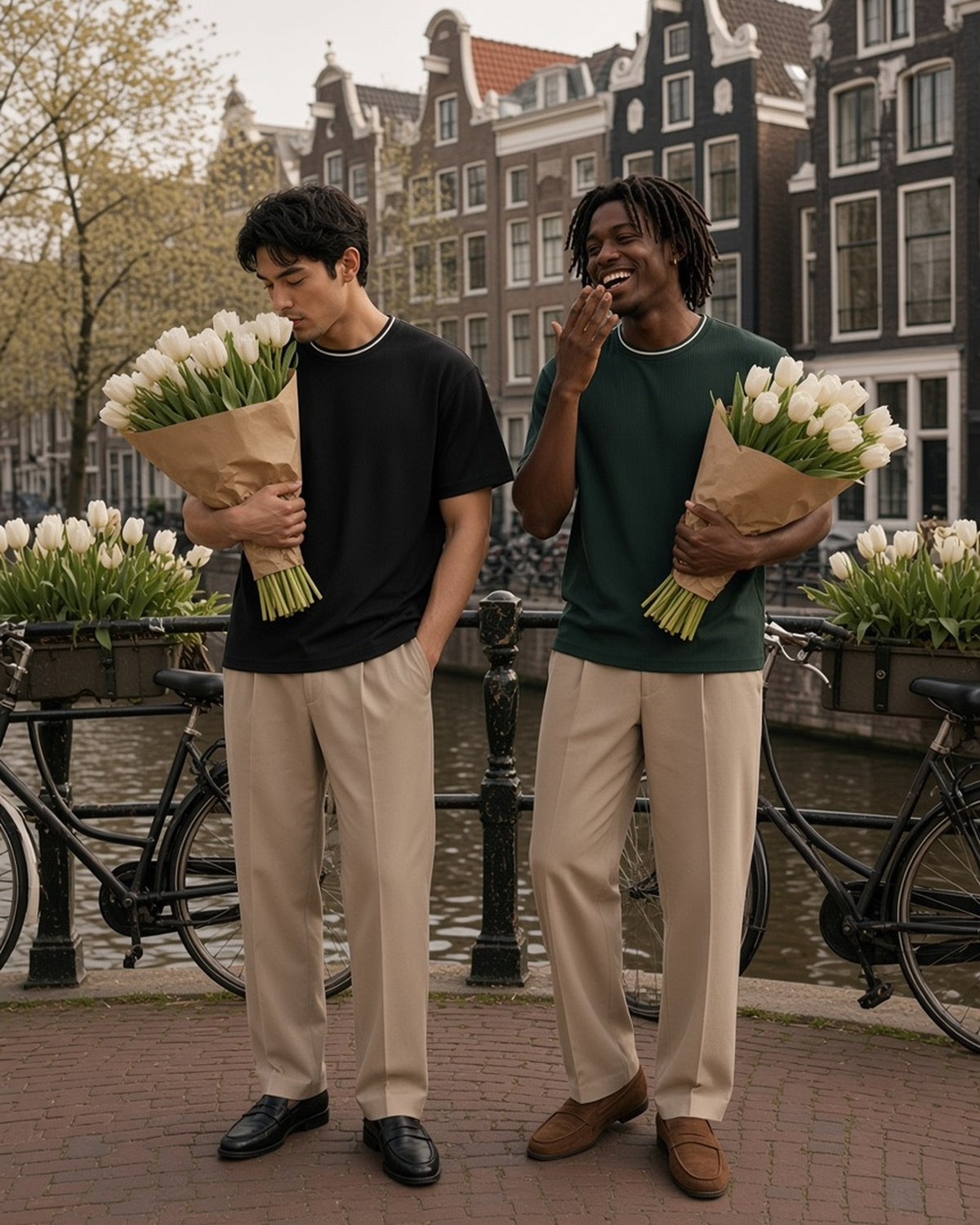 Two men in the Boxy Ribbed T-Shirt in Black and Dark Green, carrying armfuls of white tulips on an Amsterdam canal bridge