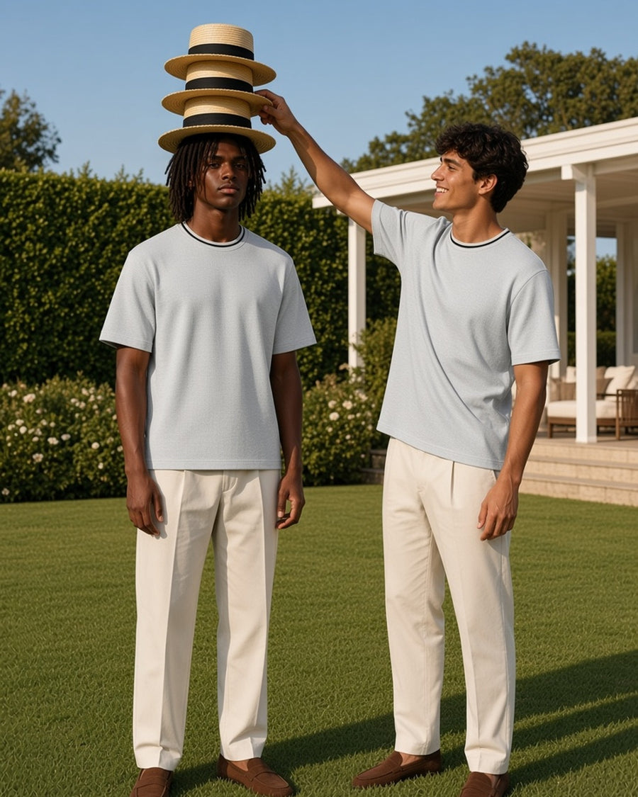 Two men in the Boxy Ribbed T-Shirt in Flower Gray, one balancing a stack of straw boaters on a club lawn