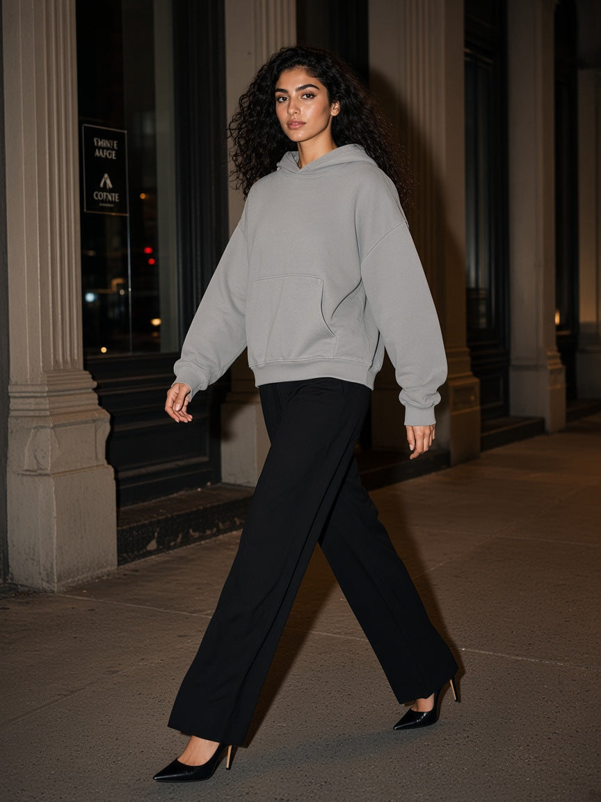 Marcel Afters Boxy Vintage Washed Hoodie in Light Gray, worn by a woman, walking past dark columns at night in a grey hoodie and black trousers
