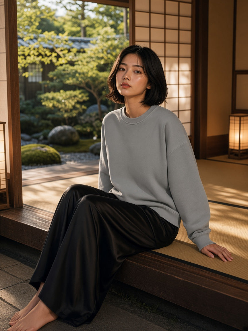 Marcel Afters Boxy Vintage Washed Sweatshirt in Light Gray, worn by a woman, seated on a tatami veranda above a Japanese garden in a black satin skirt
