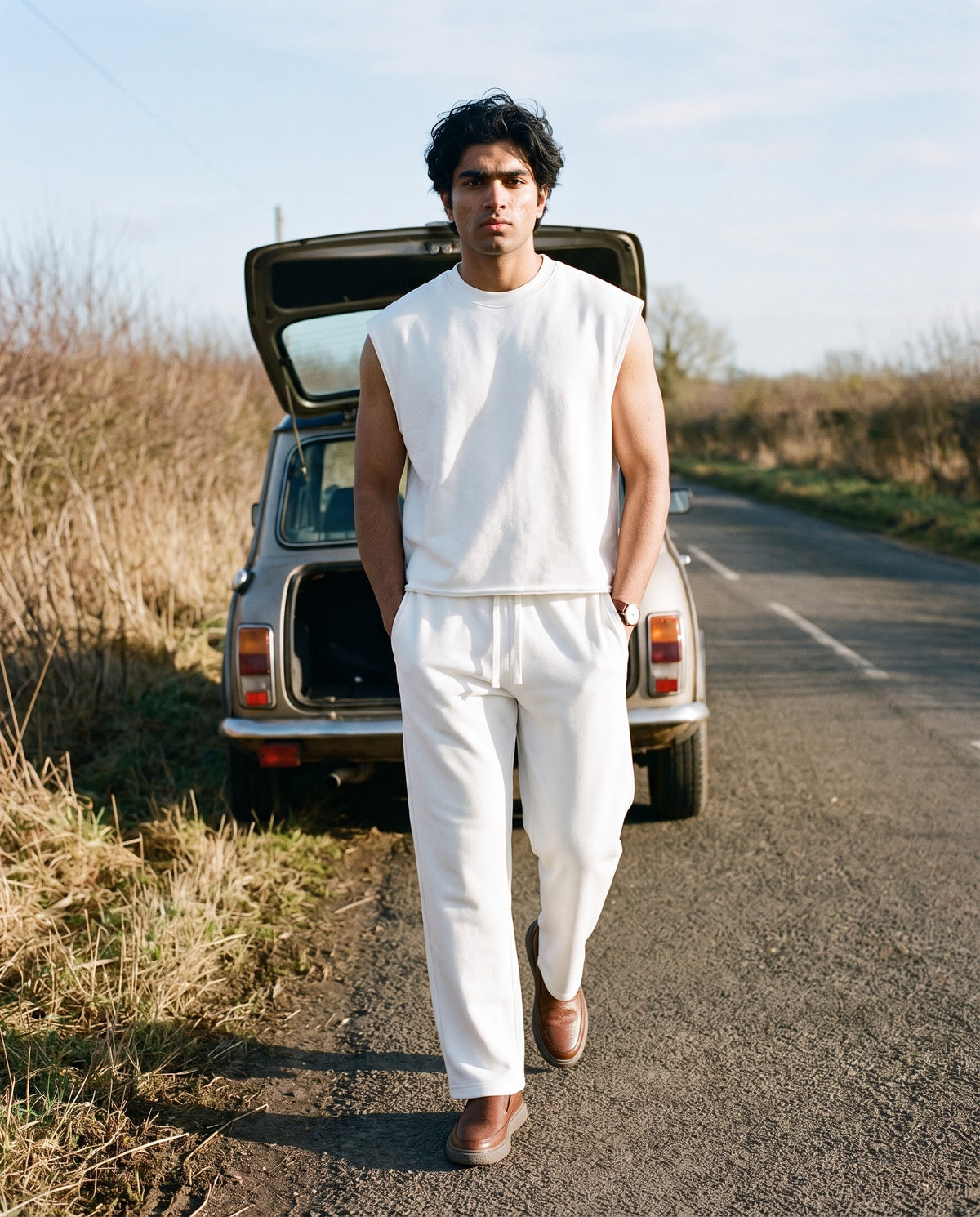 Man wearing The Day Pass Slip-On with the Men's French Terry Boxy Tank Top in White, Straight Leg Sweatpants in White. Travel Light, Autumn–Winter 2026 campaign