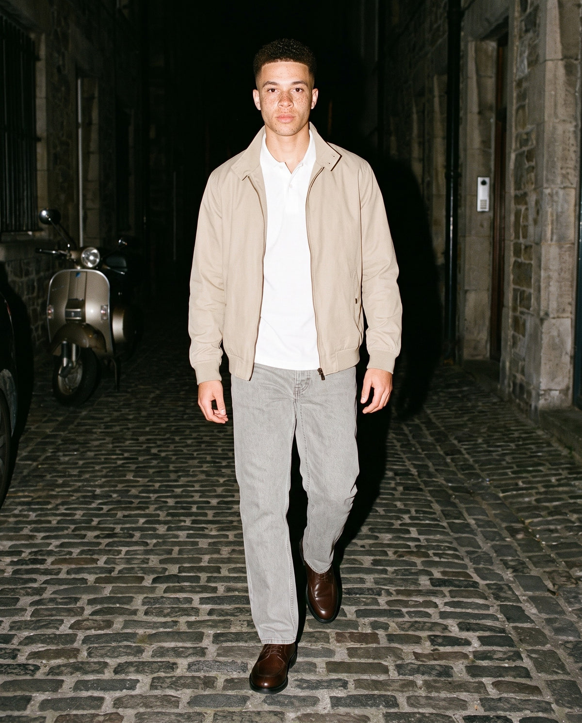 Man wearing The Wine List Derby with the Regular Fit Polo Shirt in White, Snow Washed Straight Leg Pants in Stone Gray, Stand Collar Jacket in Beige. Dinner at Nine, Autumn–Winter 2026 campaign