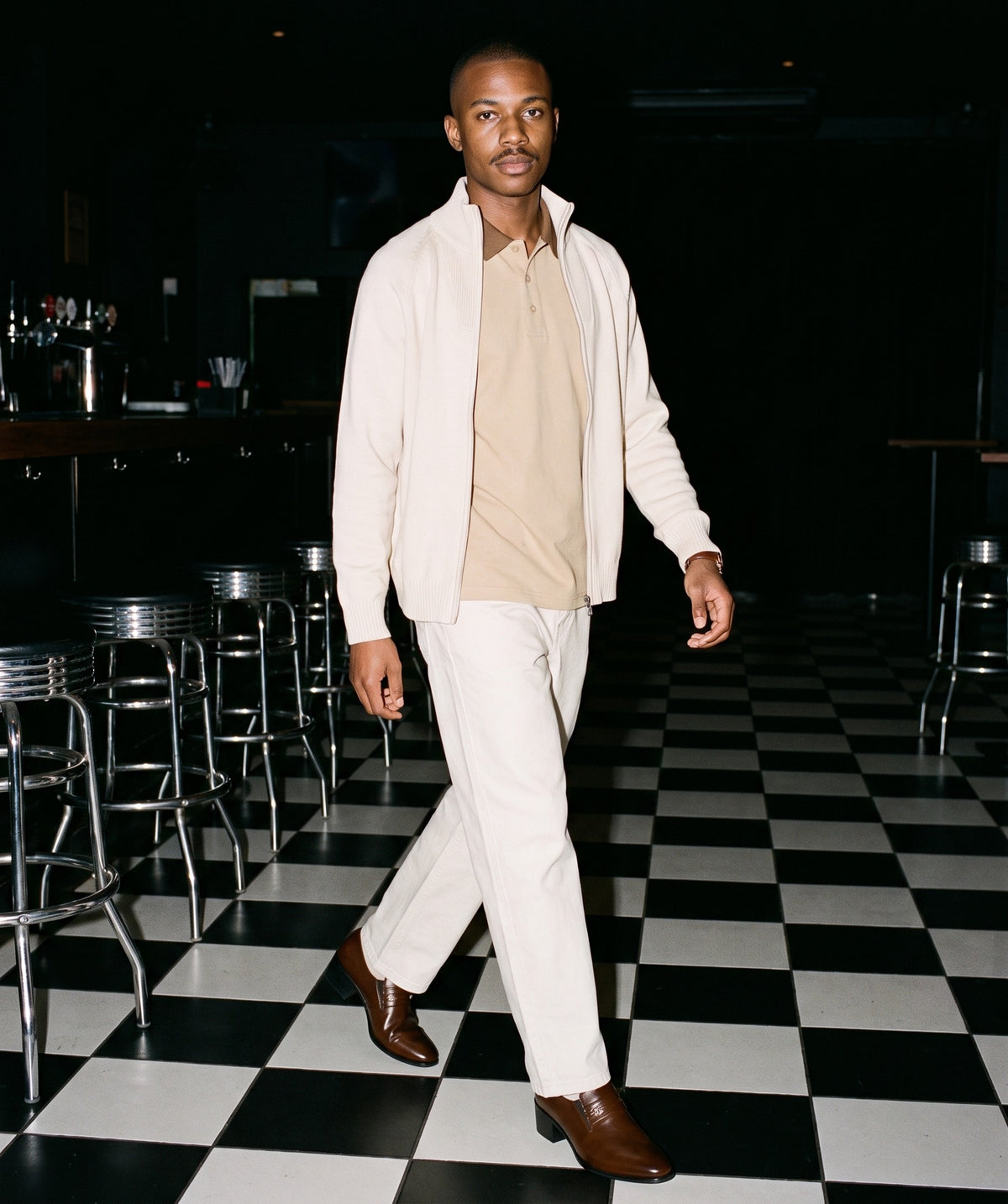 Man wearing The Aperitivo Loafer with the Contrast Collar Raglan Polo Shirt in Khaki, Heavyweight Cotton Straight-Leg Pants in Pale Khaki, Quarter-Zip Pullover Sweatshirt in Beige. After Dark, Autumn–Winter 2026 campaign