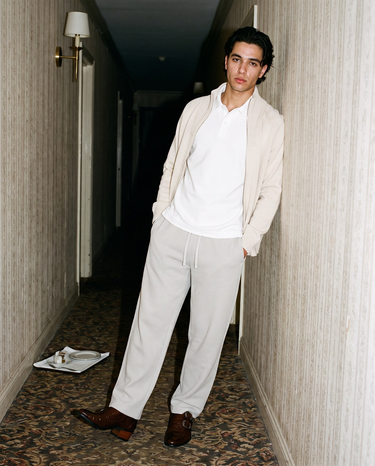Man wearing The Card Room Monk with the Drop Shoulder Short-Sleeve Polo in White, Waffle Barrel Leg Pants in Oat Gray, Heavyweight Collared Quarter-Zip in Beige. After Dark, Autumn–Winter 2026 campaign