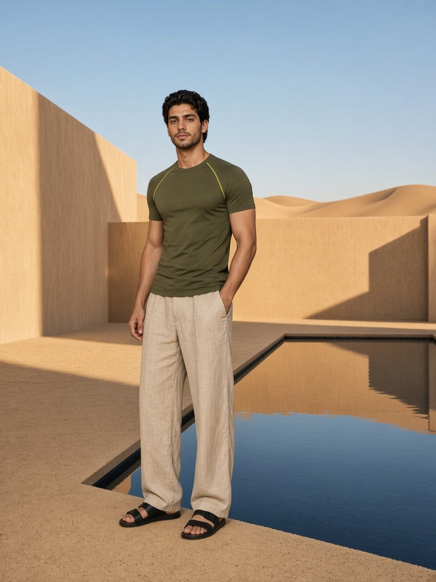 Marcel Afters Contrast Stitch Raglan T-Shirt in Army Green, worn by a man, standing beside a desert reflecting pool in linen trousers