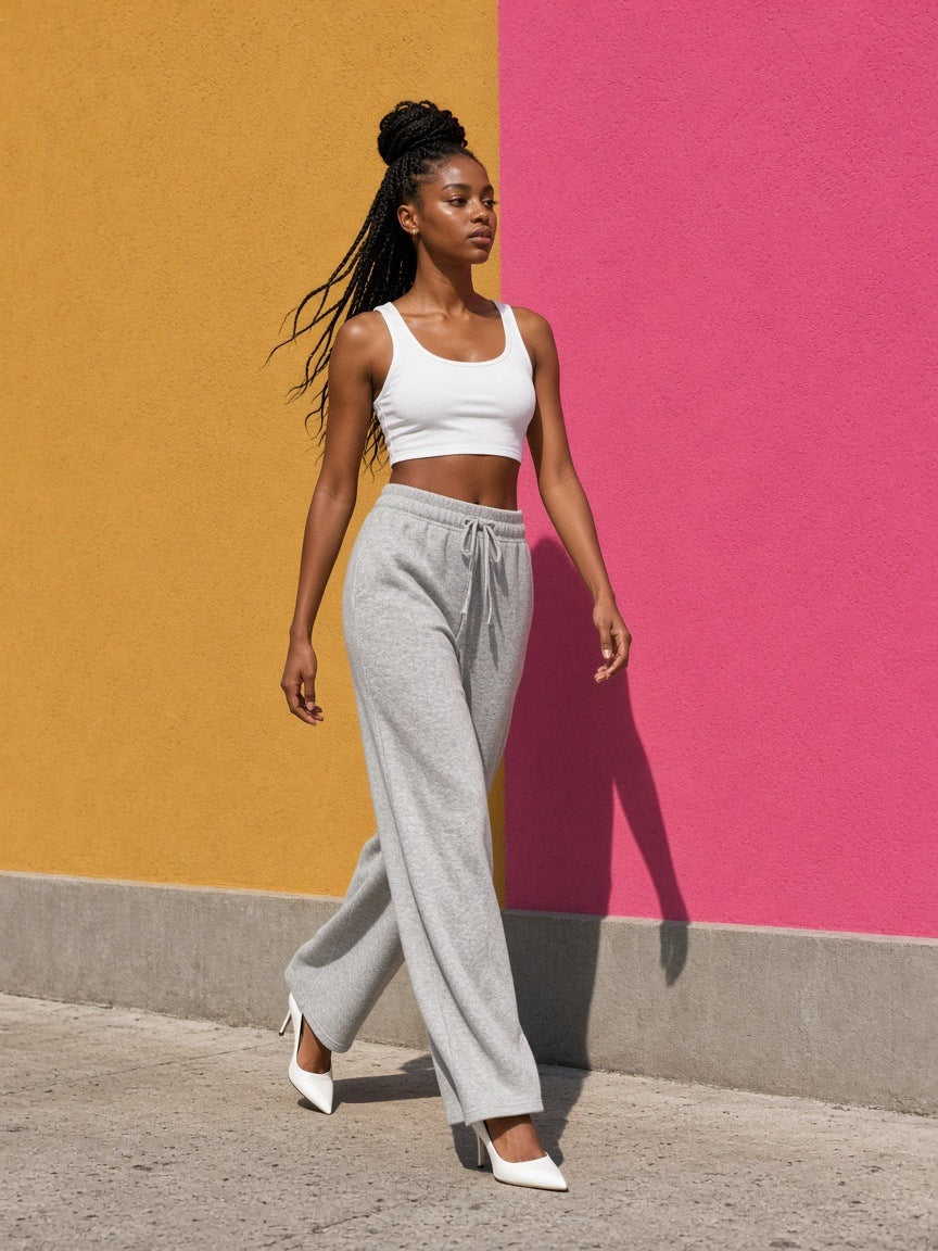 Woman in the Women's Cropped Tank Top in White with grey sweatpants and white pointed heels, walking past an ochre and pink wall