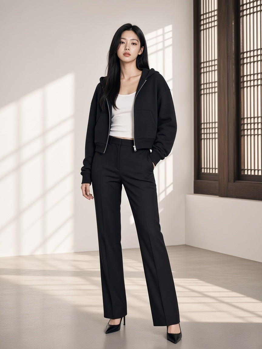 Marcel Afters Cropped Zip-Through Hoodie in Black, worn by a woman, standing by carved wooden windows in a cropped black zip hoodie and trousers