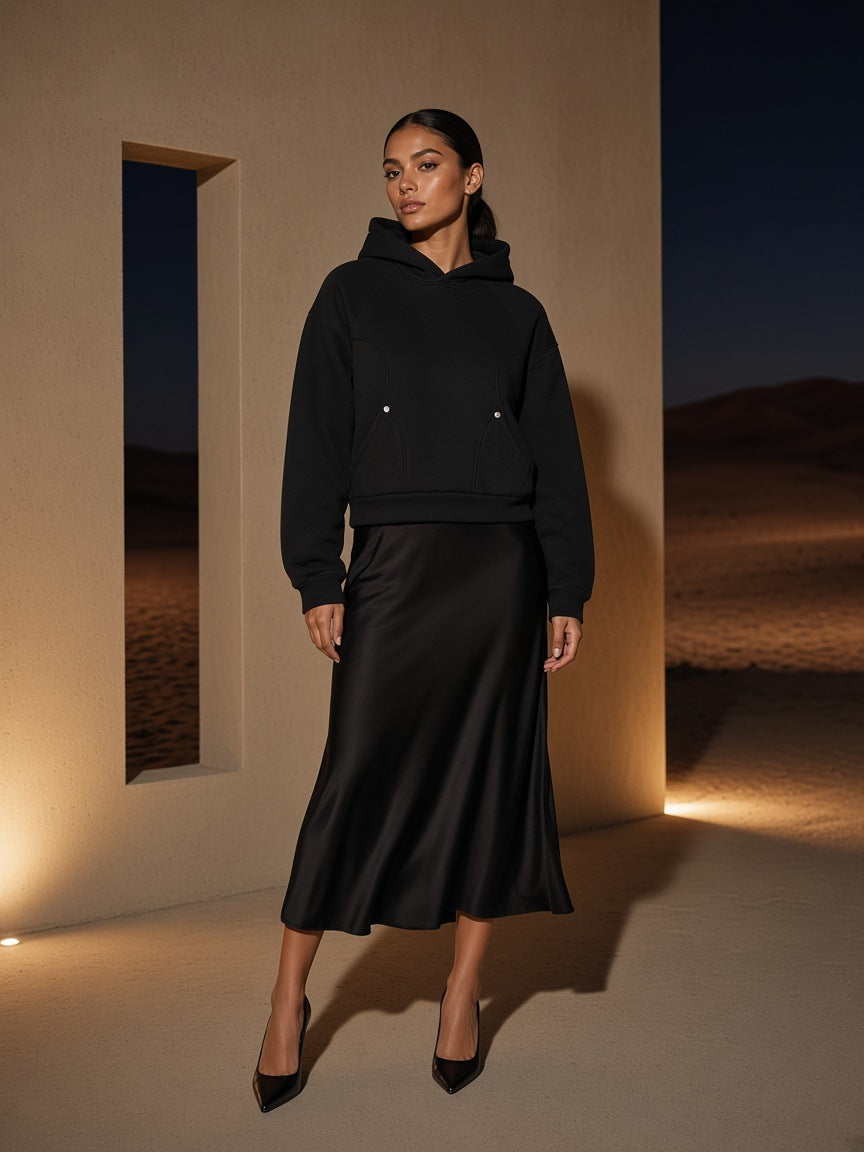 Marcel Afters Curved Panel Raglan Hoodie in Black, worn by a woman, standing in a desert-lit doorway in a long satin skirt