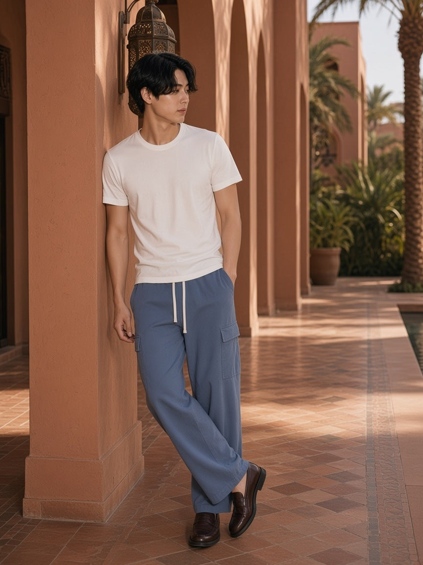Marcel Afters Drawstring Waist Straight-Leg Cargo Pants in Haze Blue, worn by a man, leaning against a terracotta arcade in a white tee