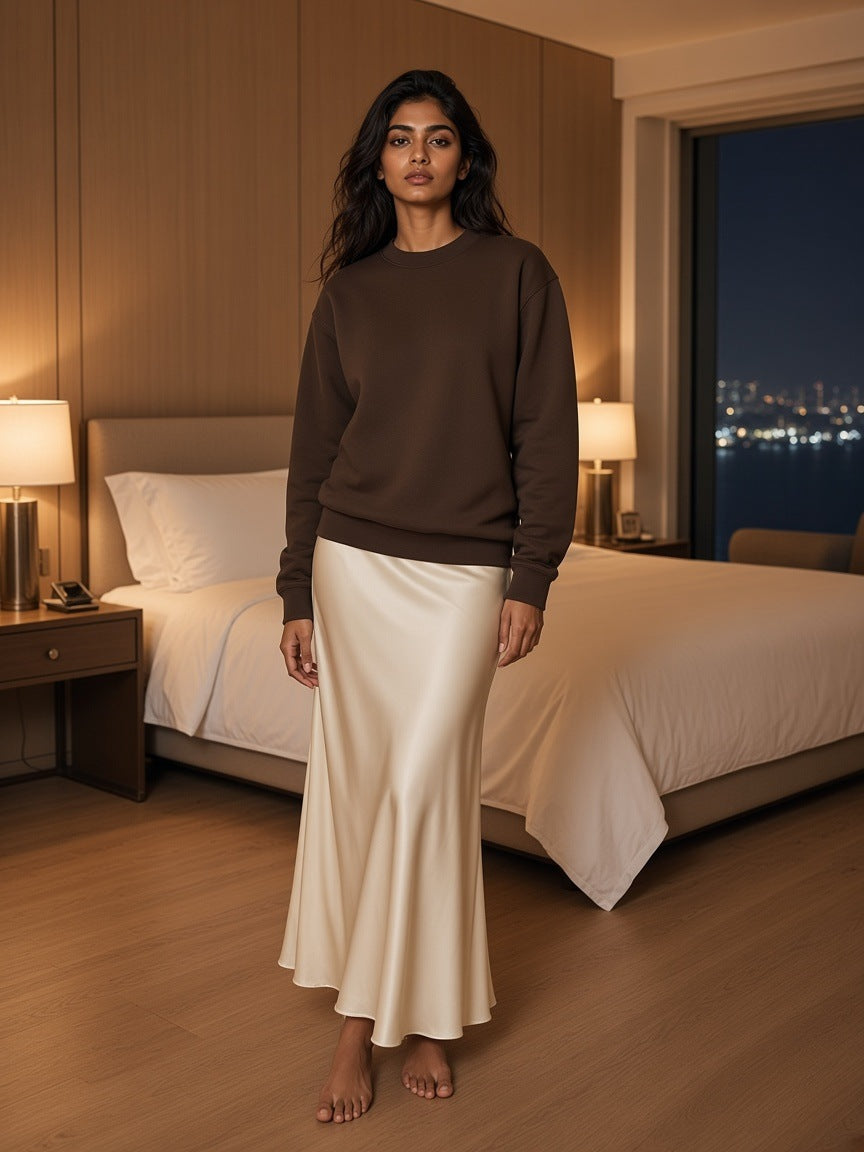 Marcel Afters Drop Shoulder Crewneck Sweatshirt in Coffee, worn by a woman, standing in a warm hotel bedroom in a satin skirt