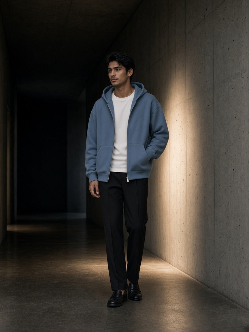 Man in a Haze Blue drop shoulder full zip hoodie over a white tee in a raw concrete corridor