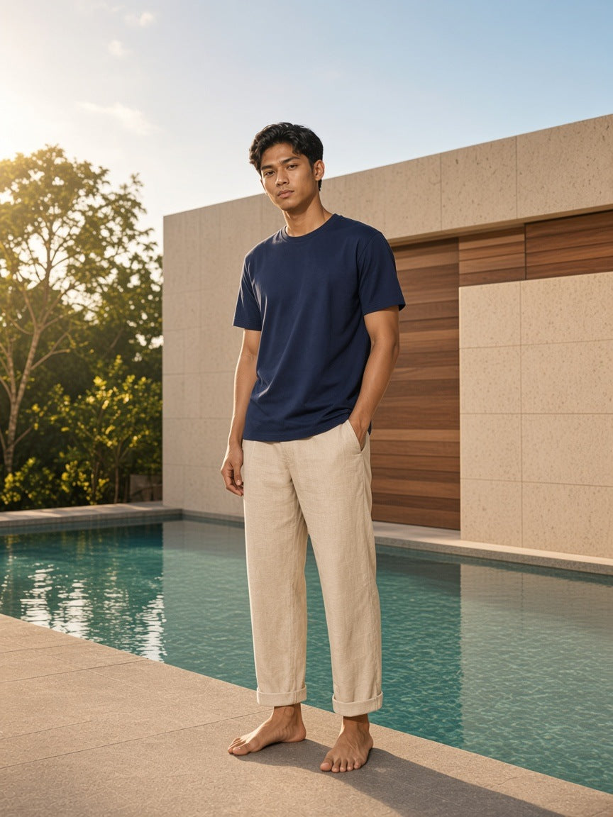 Marcel Afters Essential Cotton T-Shirt in Navy Blue, worn by a man, standing barefoot by a turquoise pool in sand trousers