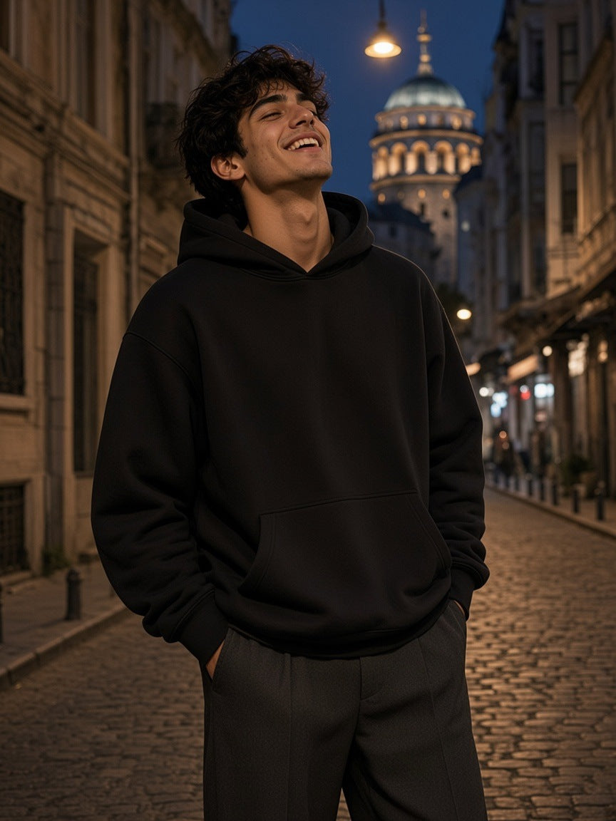 Man in the Essential Heavyweight Boxy Fleece Hoodie in Black on a cobbled street in Galata, Istanbul at night