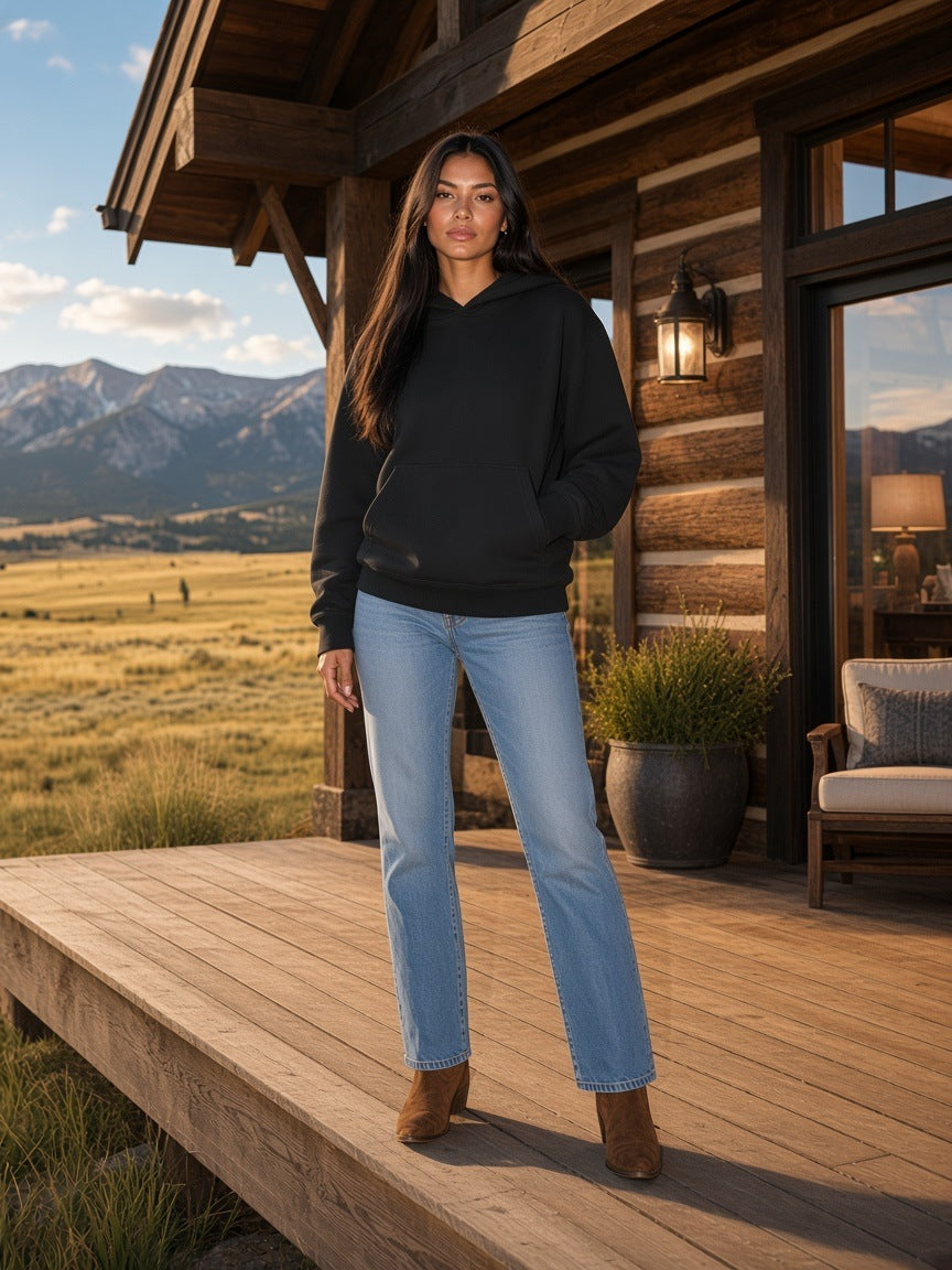 Marcel Afters Essential Heavyweight Cotton Hoodie in Black, worn by a woman, on a porch of a log cabin in a field