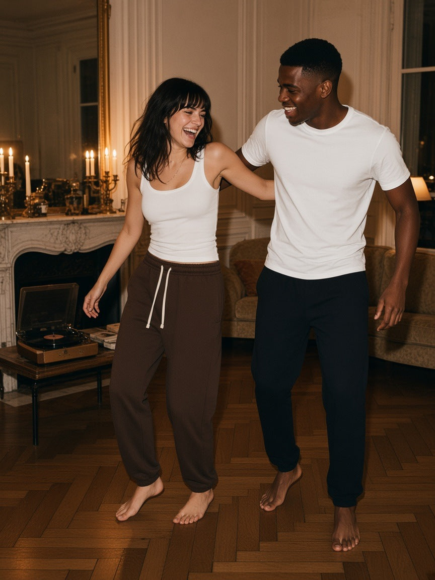 Marcel Afters Essential Heavyweight Cotton Sweatpants in Coffee, worn by a man and a woman, laughing together in a candle-lit living room, she in coffee sweatpants and he in black