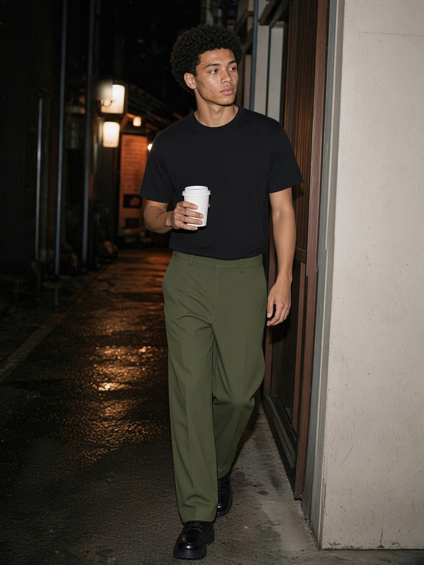 Man in the Essential Heavyweight Cotton T-Shirt in Black and olive trousers, walking a lantern-lit Tokyo alley with a coffee