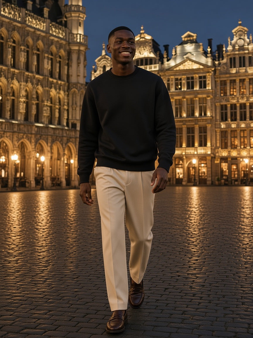 Marcel Afters Essential Heavyweight Crewneck Sweatshirt — Dark in Black, worn by a man, walking across a lit Brussels square at night