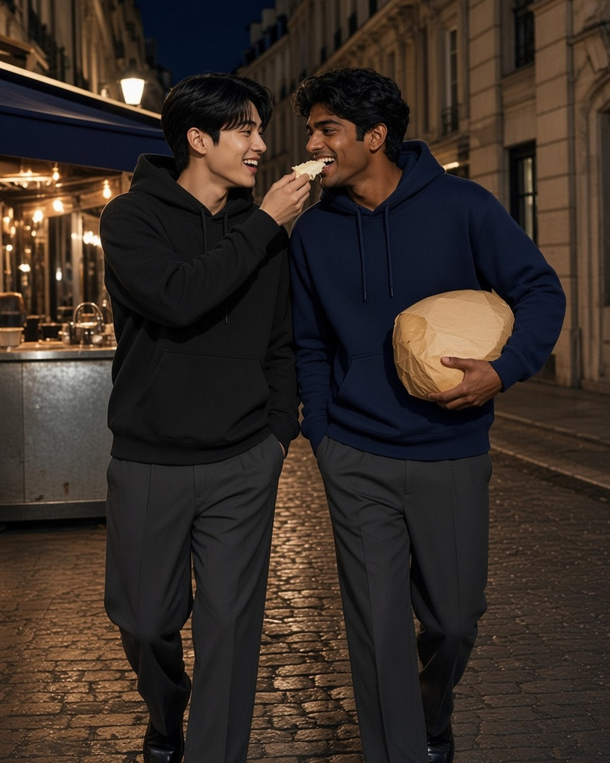 Two men in the Essential Heavyweight Drop-Shoulder Hoodie in Black and Navy Blue sharing cheese on a Paris street at night