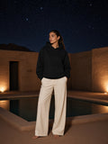 Marcel Afters Essential Heavyweight Hoodie, 400 gsm in Black, worn by a woman, standing by a lantern-lit pool at night