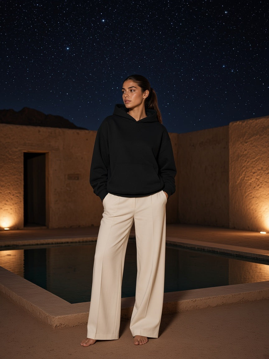 Marcel Afters Essential Heavyweight Hoodie, 400 gsm in Black, worn by a woman, standing by a lantern-lit pool at night