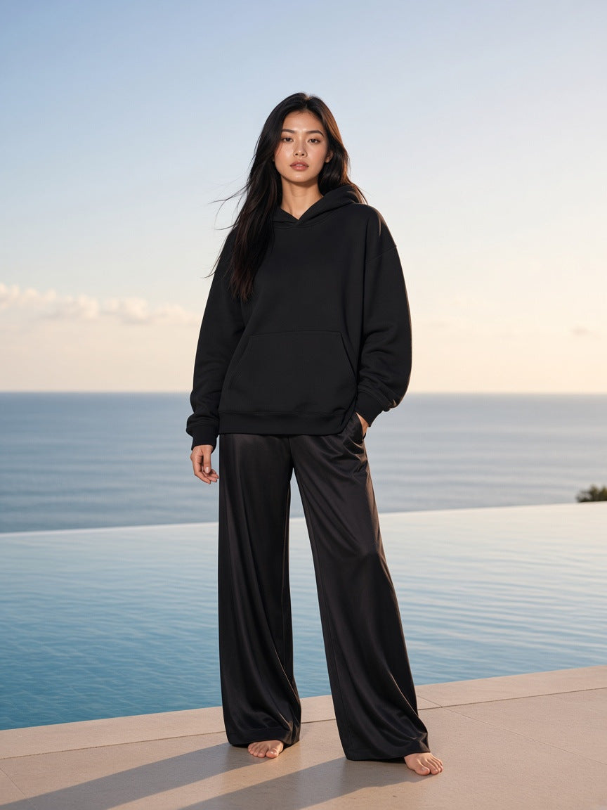 Marcel Afters Essential Heavyweight Hoodie, 400 gsm in Black, worn by a woman, standing barefoot on an infinity-pool ledge at sunset
