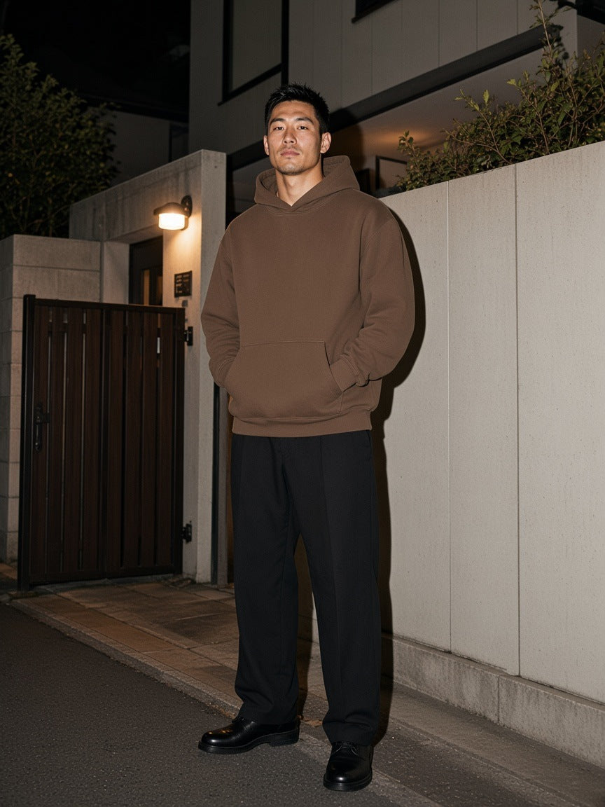 Marcel Afters Essential Heavyweight Hoodie in Coffee, worn by a man, standing beside a timber gate on a quiet street at night