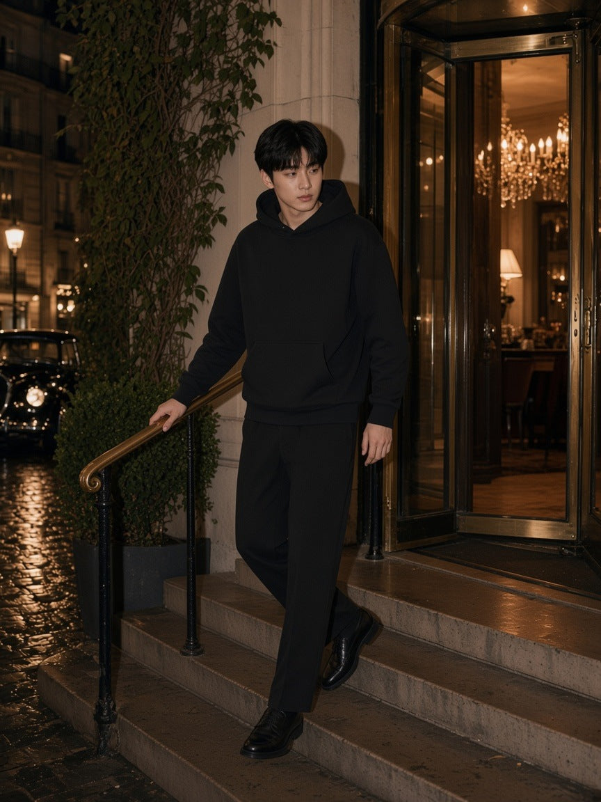 Man in the Essential Heavyweight Pocket Hoodie in Black walking down the side steps of a Paris grand hotel at night