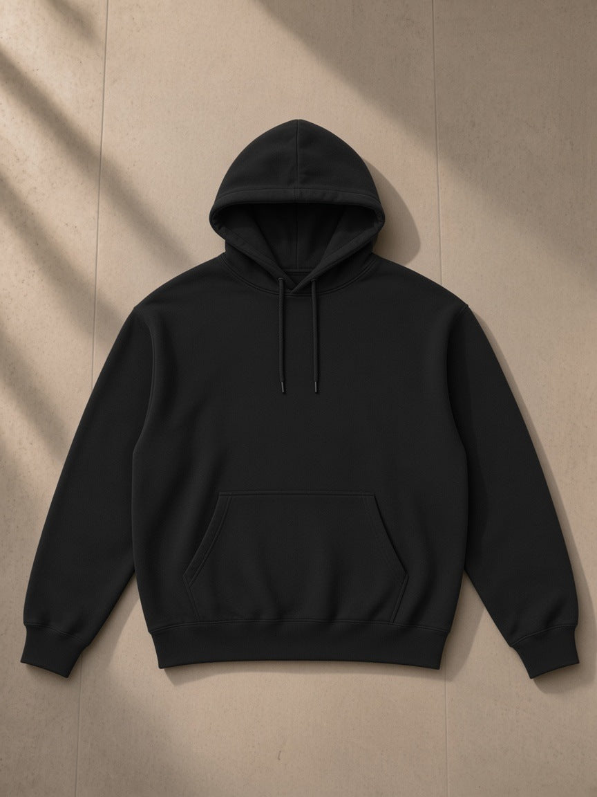 Essential heavyweight pocket hoodie in Black, laid flat on pale limestone, front view