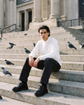 Man in White essential non-shrink mock neck sweatshirt and black jeans, seated on stone steps