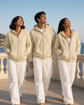 Three people in Apricot essential zip-up fleece hoodies and white trousers on a seaside terrace