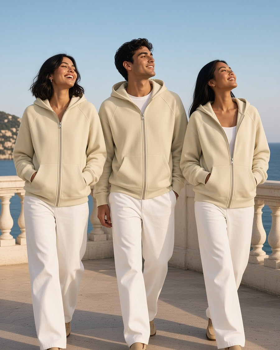 Three people in Apricot essential zip-up fleece hoodies and white trousers on a seaside terrace